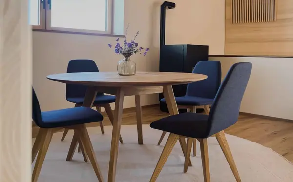 Moderner Essbereich mit rundem Holztisch, vier blauen Stühlen und Vase mit Blumen.