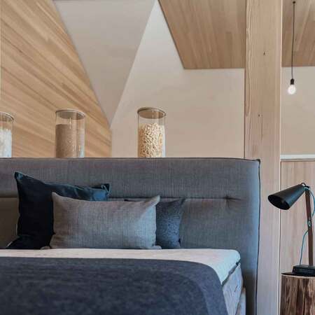 Modernes Schlafzimmer mit grauem Polsterbett, stilvollen Kissen und Holzdekor an der Decke.