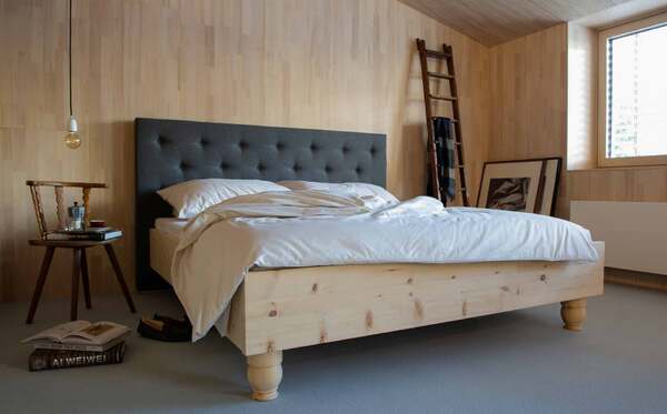 Modernes Schlafzimmer mit Massivholzbett, grauem Polsterkopfteil und natürlicher Einrichtung.