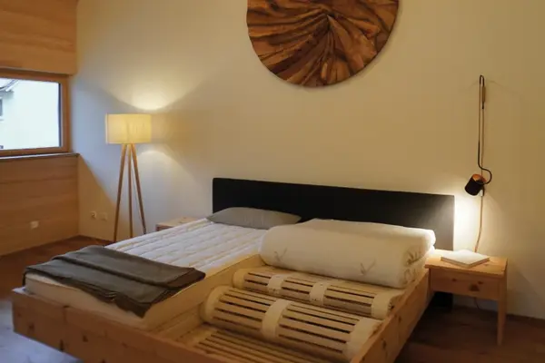 Modernes Schlafzimmer mit Holzbett, Naturmatratze, Nachttisch und stilvoller Beleuchtung.
